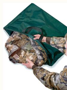 Person packing camo jacket into green bag.