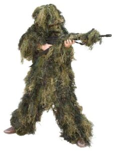 Person in camouflage ghillie suit aiming rifle.