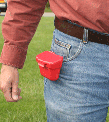Red container clipped to jeans pocket outdoors.