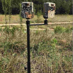 Two trail cameras mounted on a stand in field.