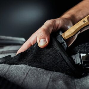 Hand securing knife in black fabric sheath.