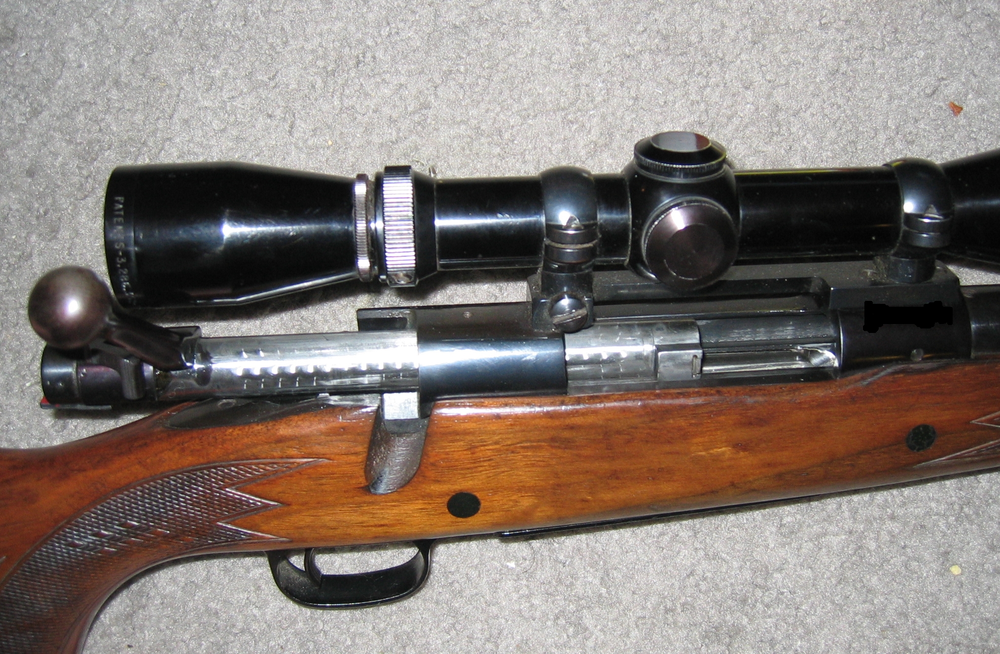Close-up of a bolt-action rifle with the bolt open, showing the short-action design